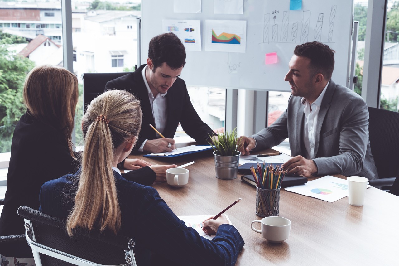 Businessman Executive In Group Meeting Discussion With Other Businessmen And Businesswomen In Modern Businessman executive in group meeting discussion with other businessmen and businesswomen in modern office with coffee cups and documents on table. People corporate business working team concept.